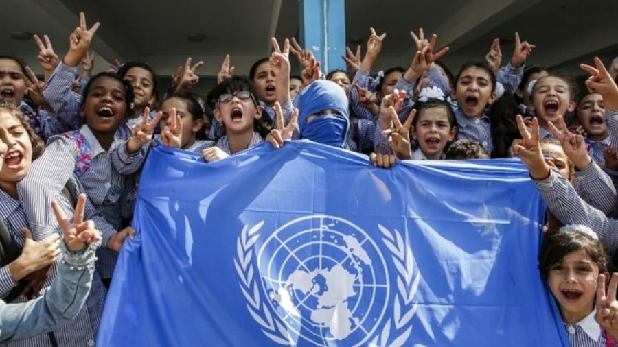Palestinian schoolchildren chant slogans over a UN flag during a protest against US aid cuts near Hebron in the occupied West Bank on 5 September 2018 (AFP)